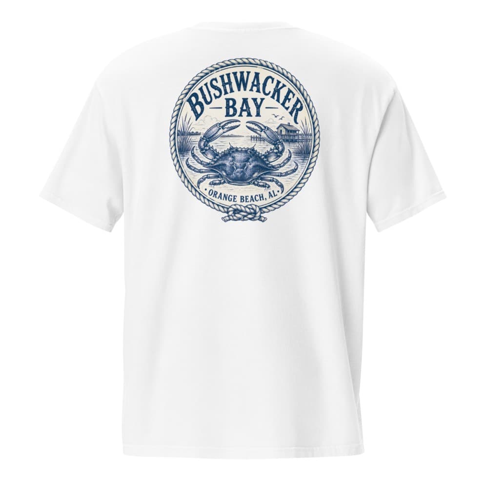 The back of a White pocket tee printed with a navy engraved crest of a blue crab over the bay, ringed in rope, with marsh grass and a stilt house on pilings behind it and Bushwacker Bay, Orange Beach, AL lettered around the ring