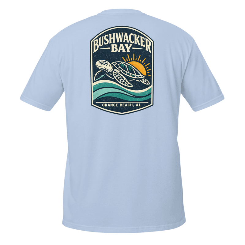The back of a tee printed with a vintage crest of a loggerhead sea turtle swimming over layered waves with the sun rising behind her, arched Bushwacker Bay lettering above and Orange Beach, AL beneath